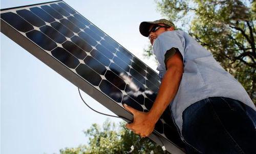 戴着帽子和眼镜的人正在吊起一块太阳能电池板